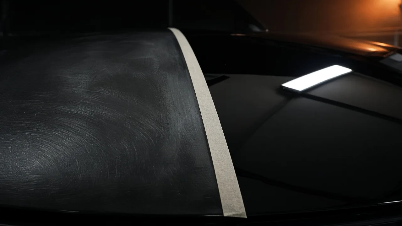 A black bonnet split by masking tape: dull swirled paint on the left, mirror-gloss corrected paint on the right