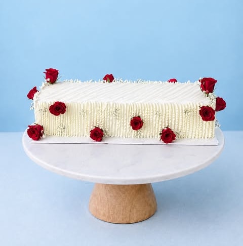 A long cream cake finished with red roses
